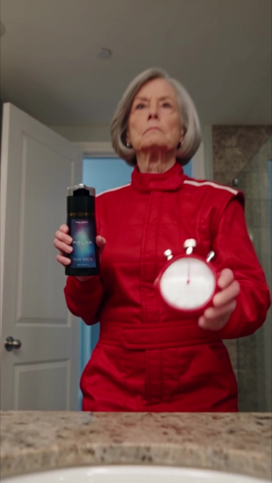 A woman in red presenting a hair-care bottle and stopwatch